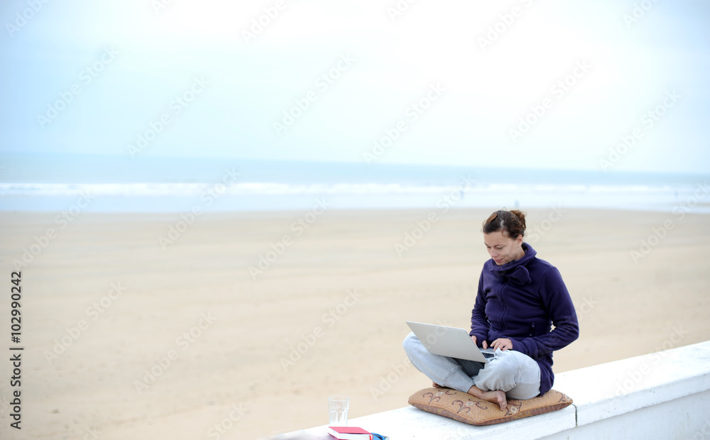 Frau mit modernem Arbeitsplatz  arbeitet am Strand am laptop 