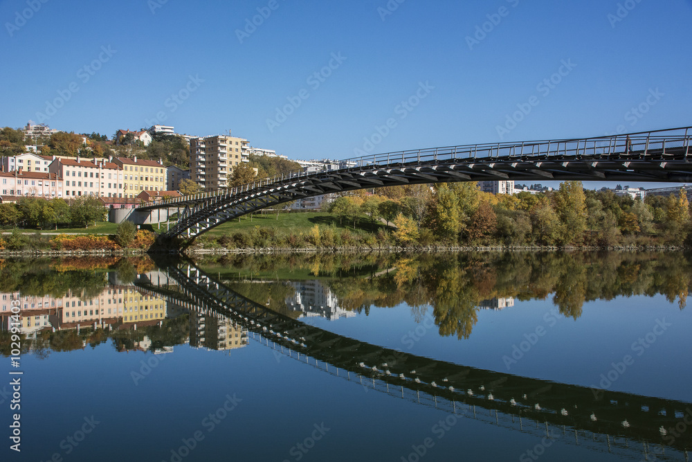 Long modern pedestrian bridge reflected in the river in autumn