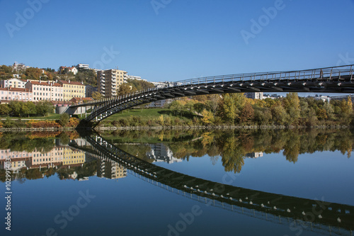 Long modern pedestrian bridge reflected in the river in autumn