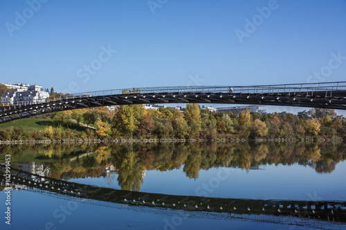 Long modern pedestrian bridge above the river with reflection
