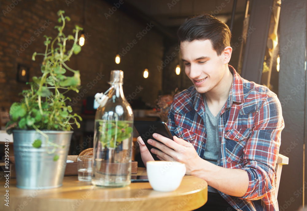 Young man sitting at a cafe, using a tablet, drinking espresso 