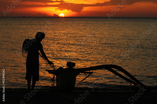 Silhouette of a fisherman and his boat on the beach. Sunset background with orange sky