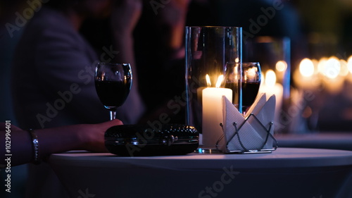 Close-up footage of elegantly decorated table at restaurant,female visitor holding a glass of red wine, fancy black clutch bag is near. 