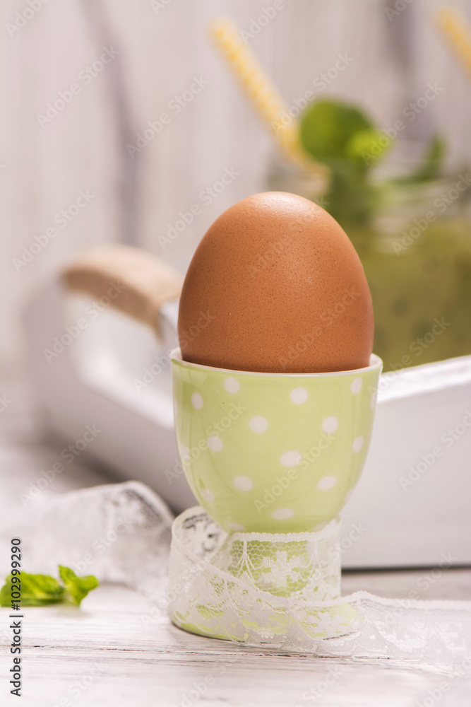 Boiled egg in an eggcup and green smoothies on white wooden table. Selective focus Boiled egg in an eggcup and green smoothies on white wooden table. Selective focus