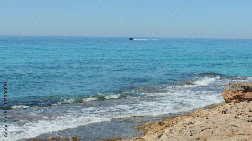 Cap De Ses Salines - the south cape of Majorca Island. Red stones and serene turquoise sea. Boat is coming from the distance. Cap De Ses Salines - the south cape of Majorca Island. Red stones and serene turquoise sea. Boat is coming from the distance.