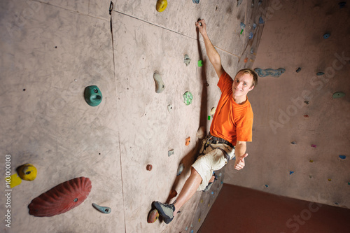 Young man climbing on practical wall in gym
