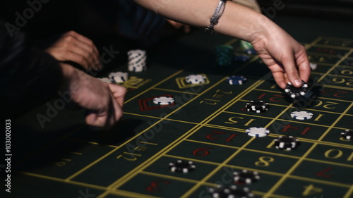 Close-up footage of hands of adult people placing their bets on a roulette table in casino