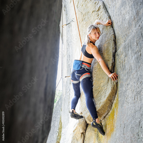 Blonde cute climber climbing with rope natural rock wall