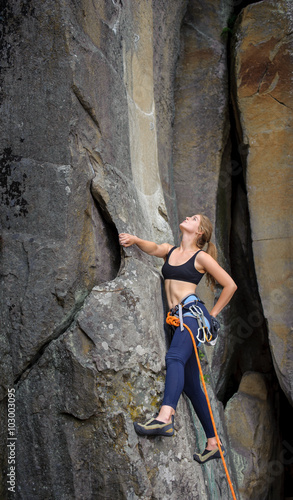 Young beautiful female climber climbing with rope on a steep roc