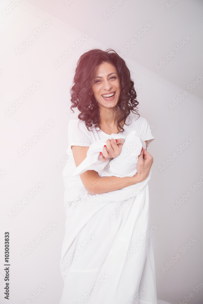 Brunette woman covered by white duvet on hite bed Brunette woman covered by white duvet on hite bed
