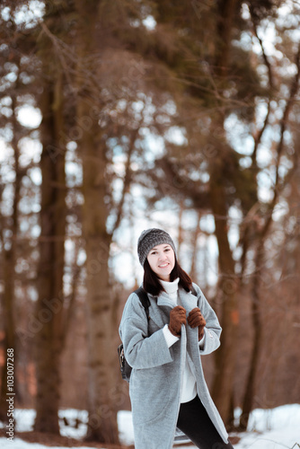 Portrait of a happy beautiful girl with brown hair in winter forest.Attractive brunette woman dressed in a hipster style with black stylish leather backpack wearing grey coat and white pullover.