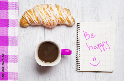 Cup of coffee with fresh croissant and paper notes on wooden background photo