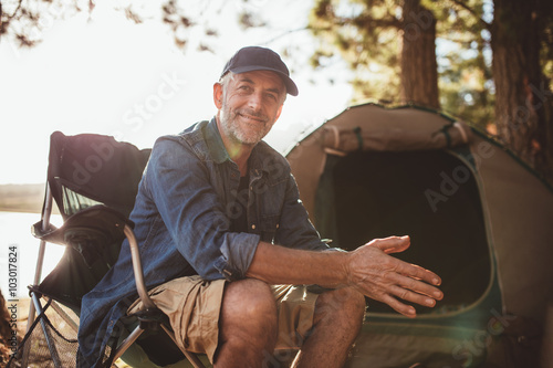 Happy mature man sitting in front of a tent