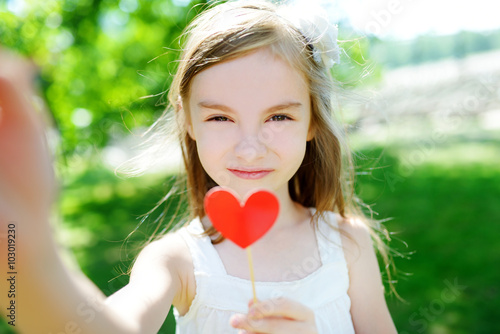 Adorable little girl playing with paper heart on a stick