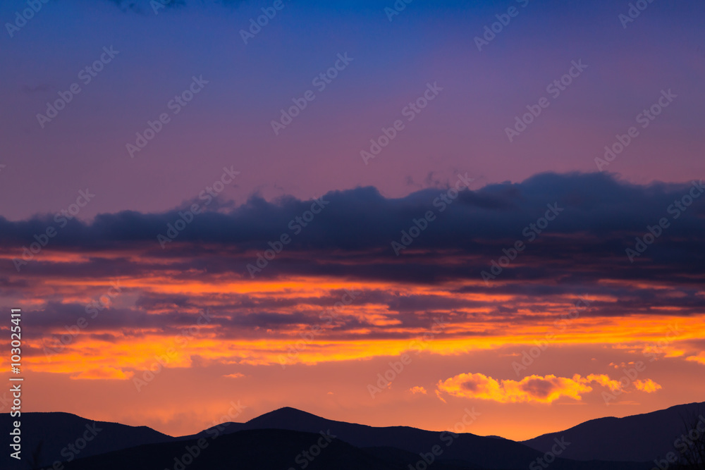 Majestic vivid sunset/sunrise with clouds over dark mountains silhouettes