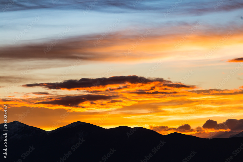 Majestic vivid sunset/sunrise with clouds over dark mountains silhouettes