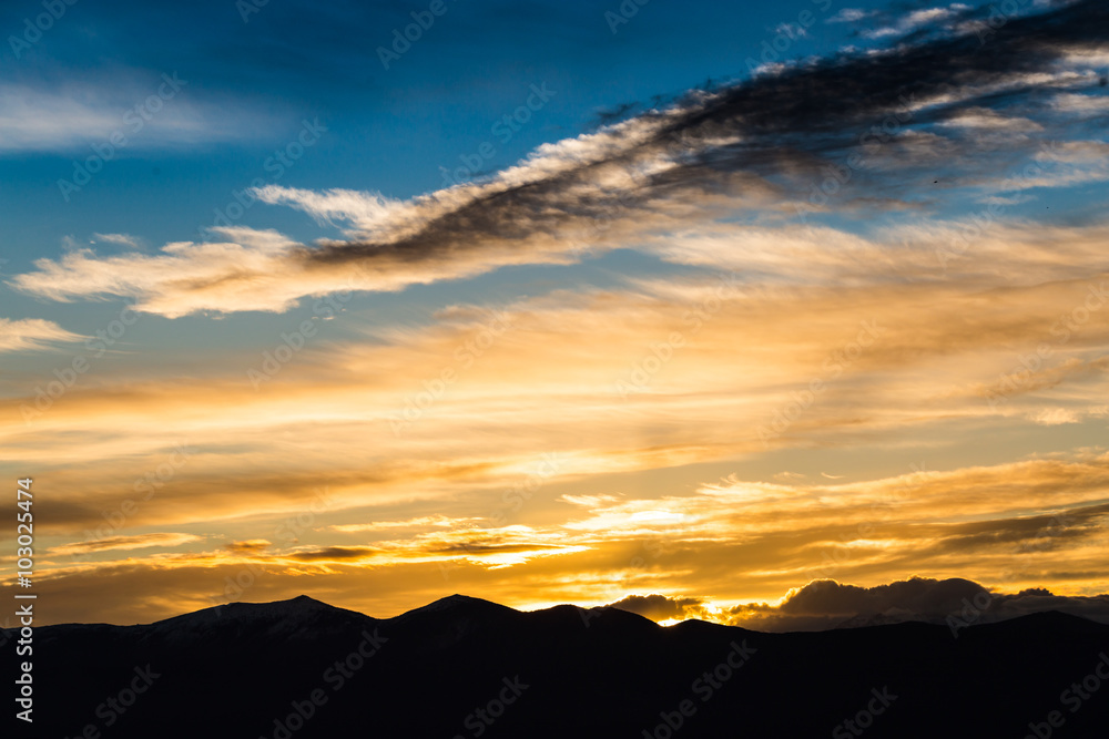 Fototapeta premium Majestic vivid sunset/sunrise with clouds over dark mountains silhouettes