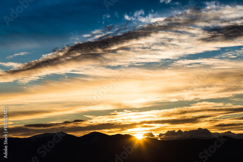 Majestic vivid sunset/sunrise with clouds over dark mountains silhouettes