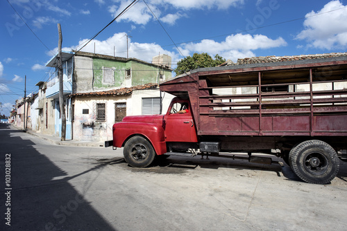 Kuba, Camagüey: Alter roter LKW parkt auf der Strasse der kubanischen Kleinstadt mit kleinen Häusern und blauem Himmel im Hintergrund