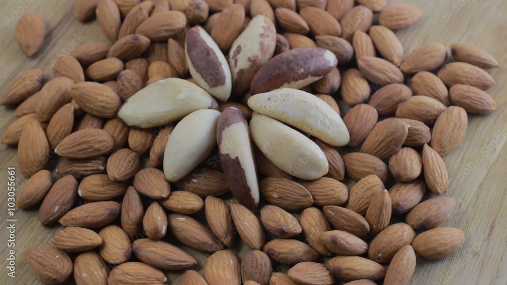 Close up shot of a pile of almonds and brazilian nuts rotating on wooden table Close up shot of a pile of almonds and brazilian nuts rotating on wooden table