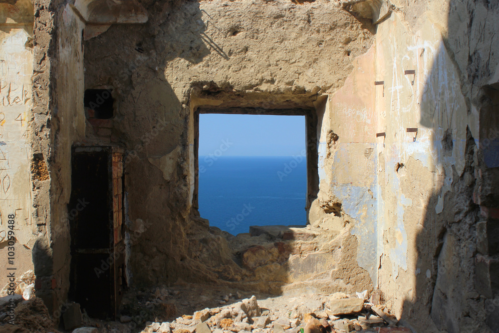Embrasure window in the wall of old fortress. Blue sea and horizon are visible