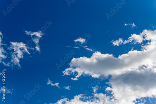 Airplane trace against blue sky and white clouds background