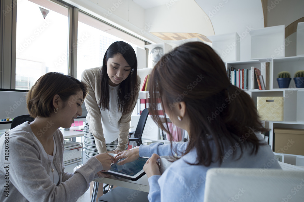Fototapeta premium Three women are talking while looking at the tablet in the office