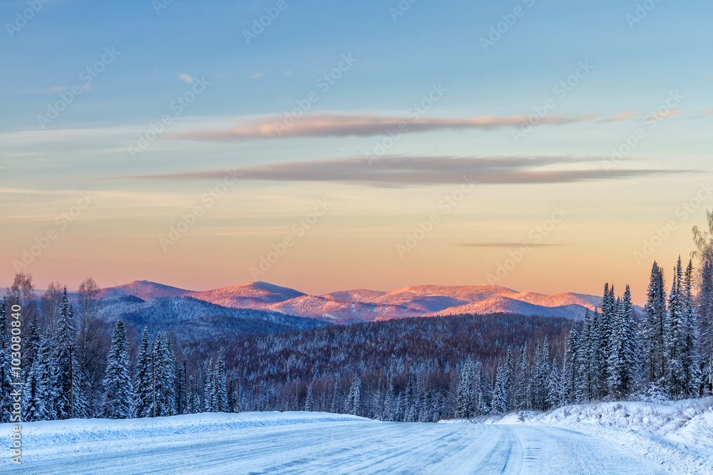 Winter road in mountains ,forest and mountain peaks in background at sunrise in Sheregesh, Siberia Winter road in mountains ,forest and mountain peaks in background at sunrise in Sheregesh, Siberia