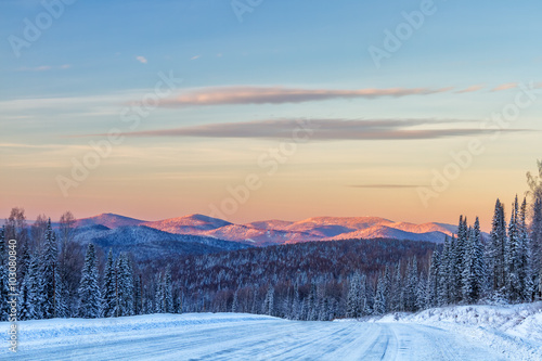 Winter road in mountains  forest and mountain peaks in background at sunrise in Sheregesh  Siberia