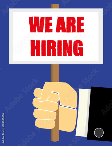 Business man hand in a suit holding a sign or placard with the phrase We Are Hiring in red text