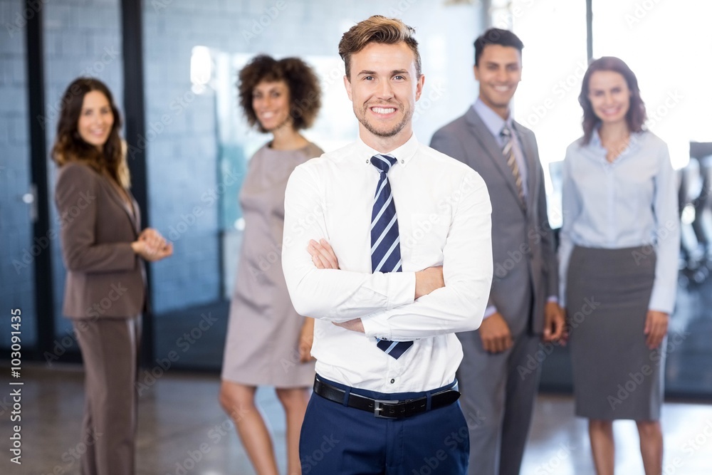 Businessman smiling at camera while his colleagues posing in bac Businessman smiling at camera while his colleagues posing in bac
