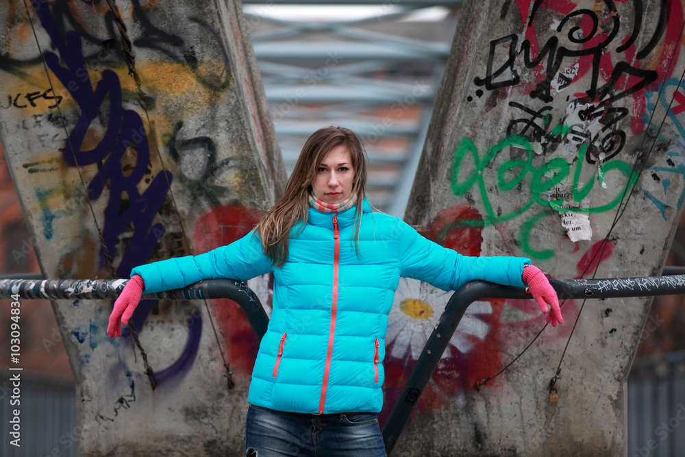 Obraz premium Beautiful blonde woman wearing jacket and pink gloves standing in front of graffiti