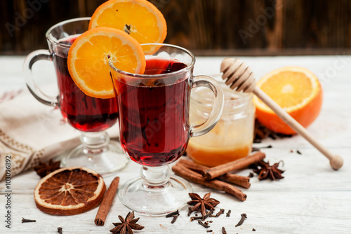 
mulled wine with oranges , honey , cinnamon and cloves on a wooden background   