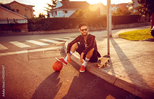 Young stylish man with a basketball and skateboard sitting on a