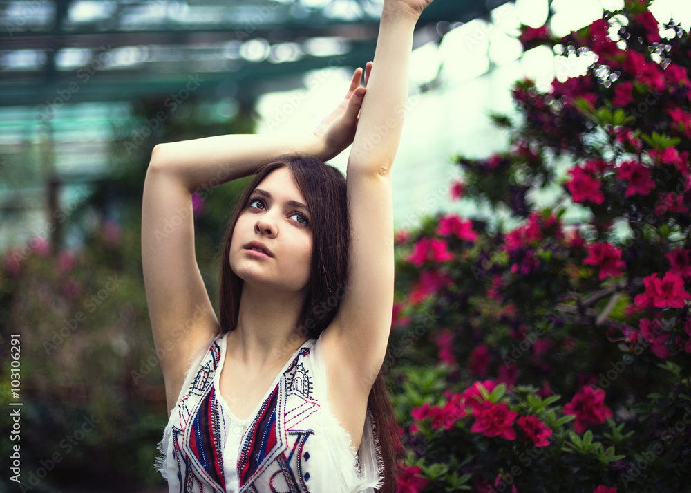 Naklejka premium Young pretty girl posing near beautiful leaves and flowers