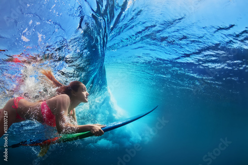 Young girl in bikini - surfer with surf board dive underwater under big ocean wave Family lifestyle, people water sport adventure camp and beach extreme swimming activity on summer vacation with child