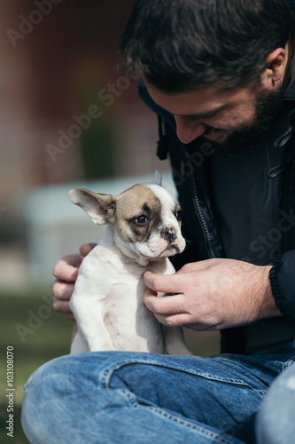 Handsome, bearded, middle age man enjoying outdoors with his adorable French bulldog puppy. City park in background.
