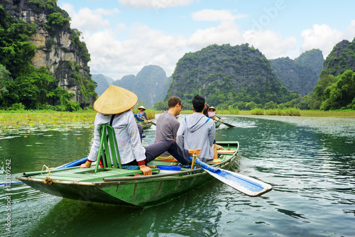 Tourists in boat. Rower using her feet to propel oars, Vietnam