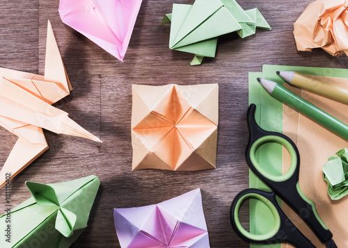 Origami figures, scissors and pencils on wooden table - flat lay, high angle.