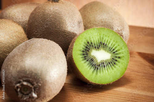 Rustic image of a bunch of kiwi fruits with one of them sliced in half showing the delicious green interior and the seeds