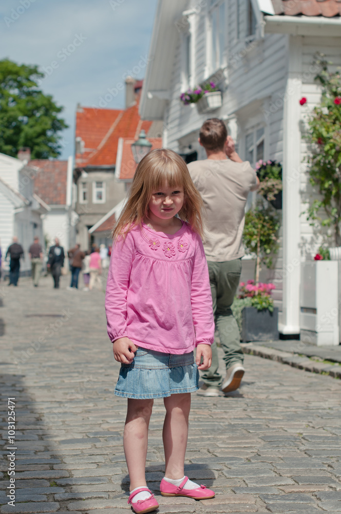 A little girl in pink on a summer street among white wooden houses