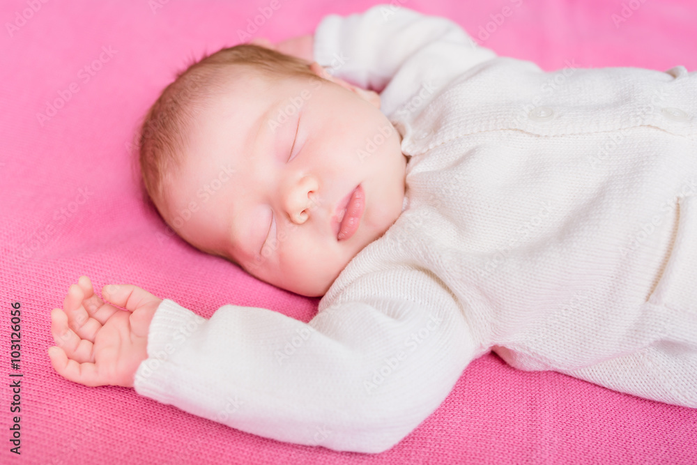 Cute little baby with closed eyes wearing knitted white clothes lying on pink plaid. 2 week old baby sleeping on pink sofa. Security and childcare concept Cute little baby with closed eyes wearing knitted white clothes lying on pink plaid. 2 week old baby sleeping on pink sofa. Security and childcare concept