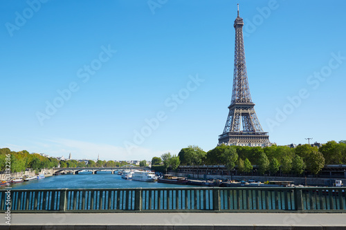 Eiffel tower and empty sidewalk bridge on Seine river, clear blue sky