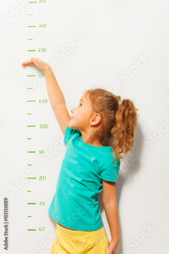 Little girl pretend how high she is on wall scale