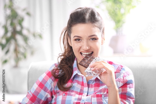 Portrait of beautiful young brunette with chocolate on sofa in the room , close up