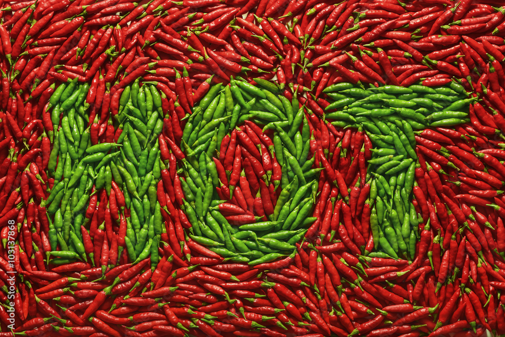 Word HOT written with green peppers, amid red peppers.