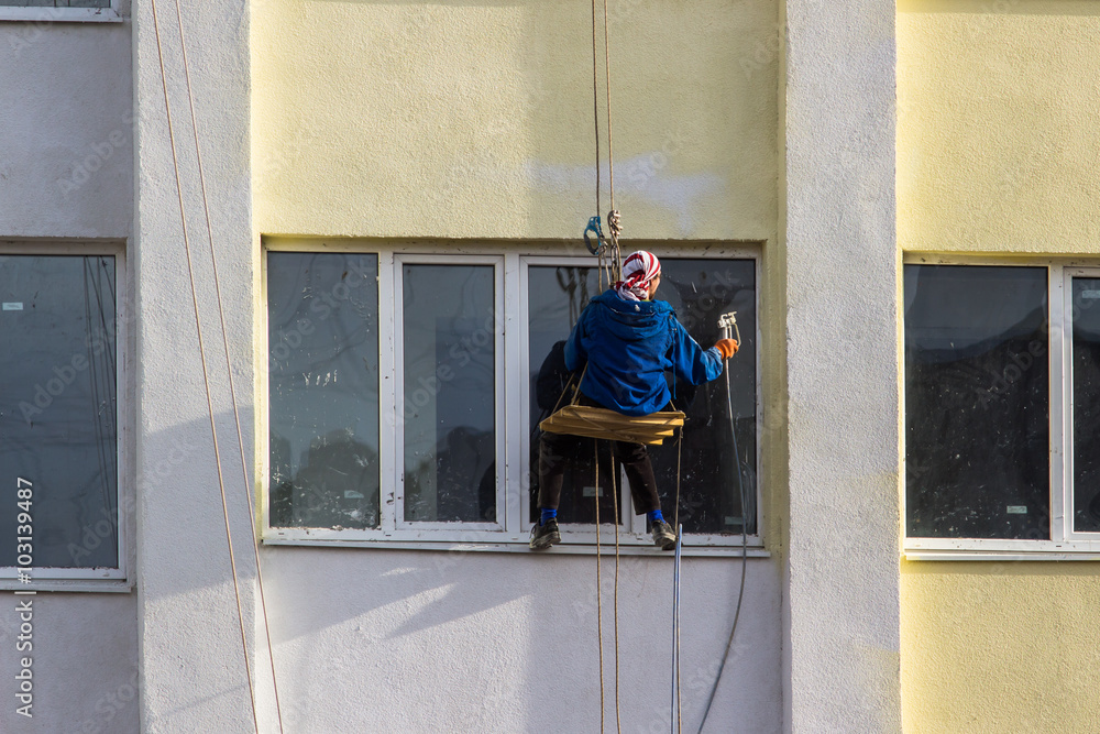 Man works at height, paint spray exterior of a building
