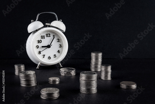 Vintage alarm clock showing 9 o'clock and coin towers on black background. Time is money business concept