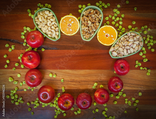 Apples, oranges, pistachios, walnuts, cashews, and wasabi peas on wooden table. Top view