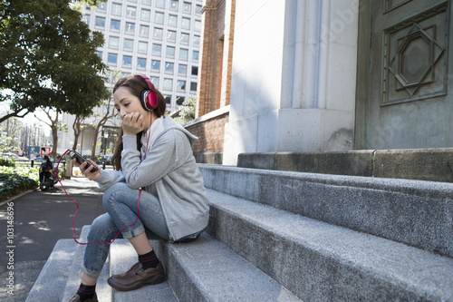 Women are listening to music with headphones sitting on the outside of the stairs #103148696